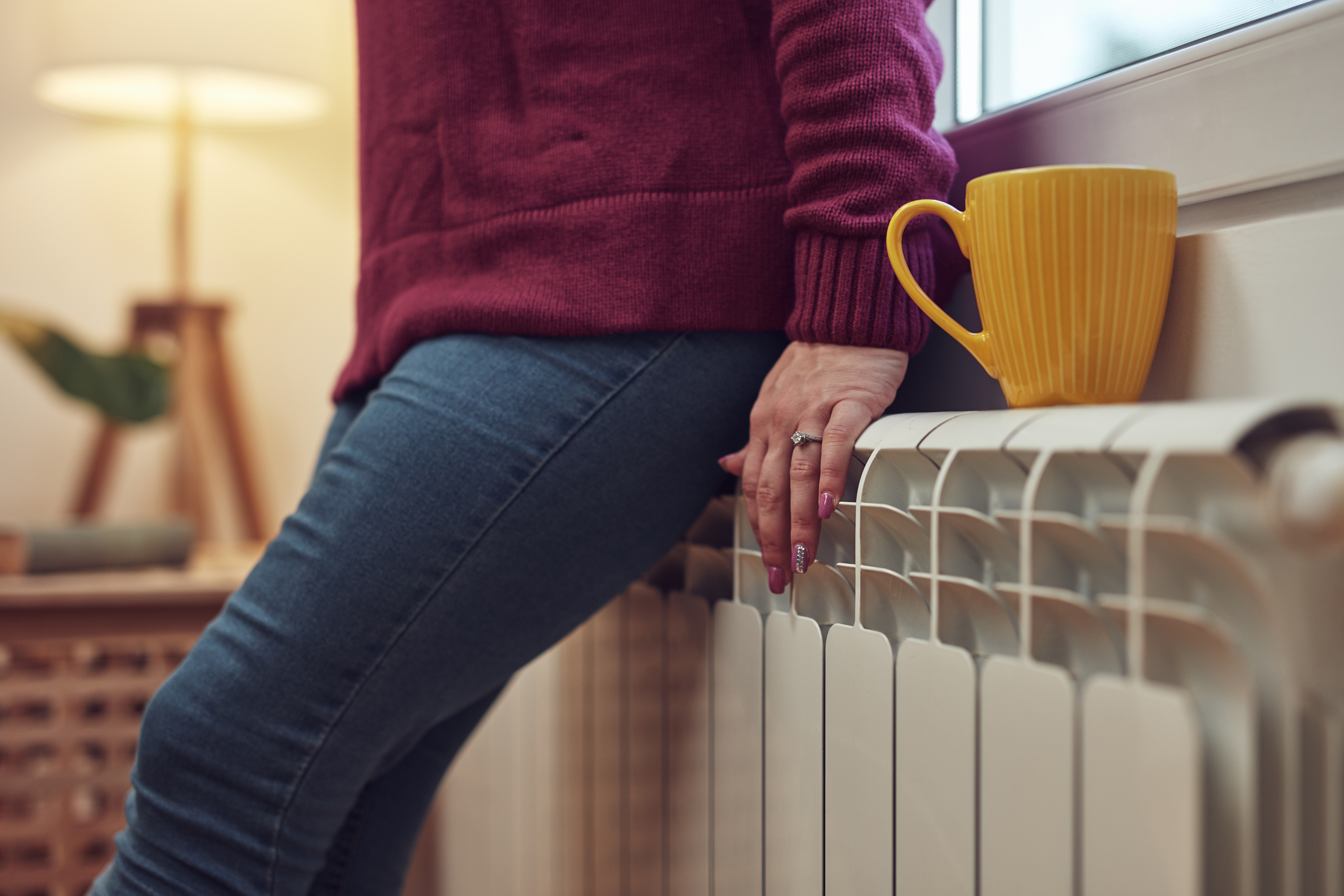 woman leaning against furnace heating system with a cup of coffee